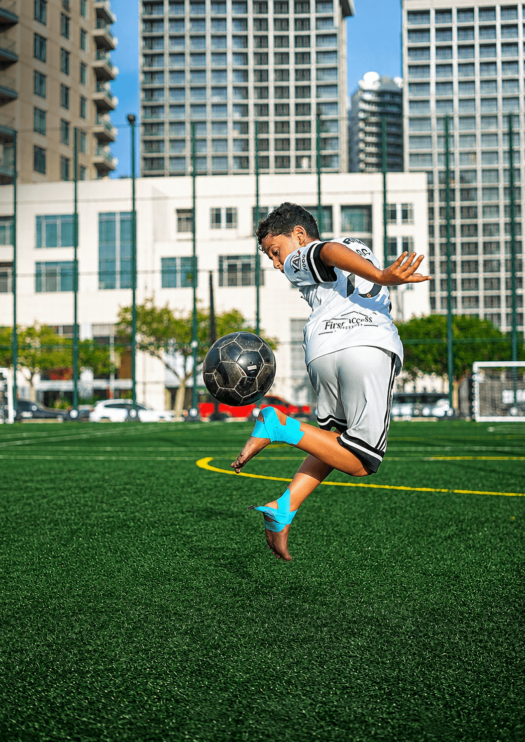 A player volleying the ball mid-air on the training pitch, Dubai towers behind