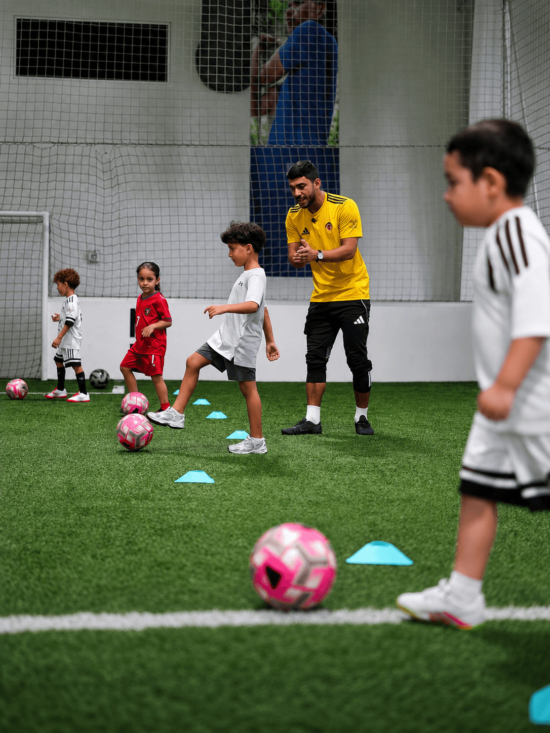Young players working a cone drill with their coach on the covered pitch