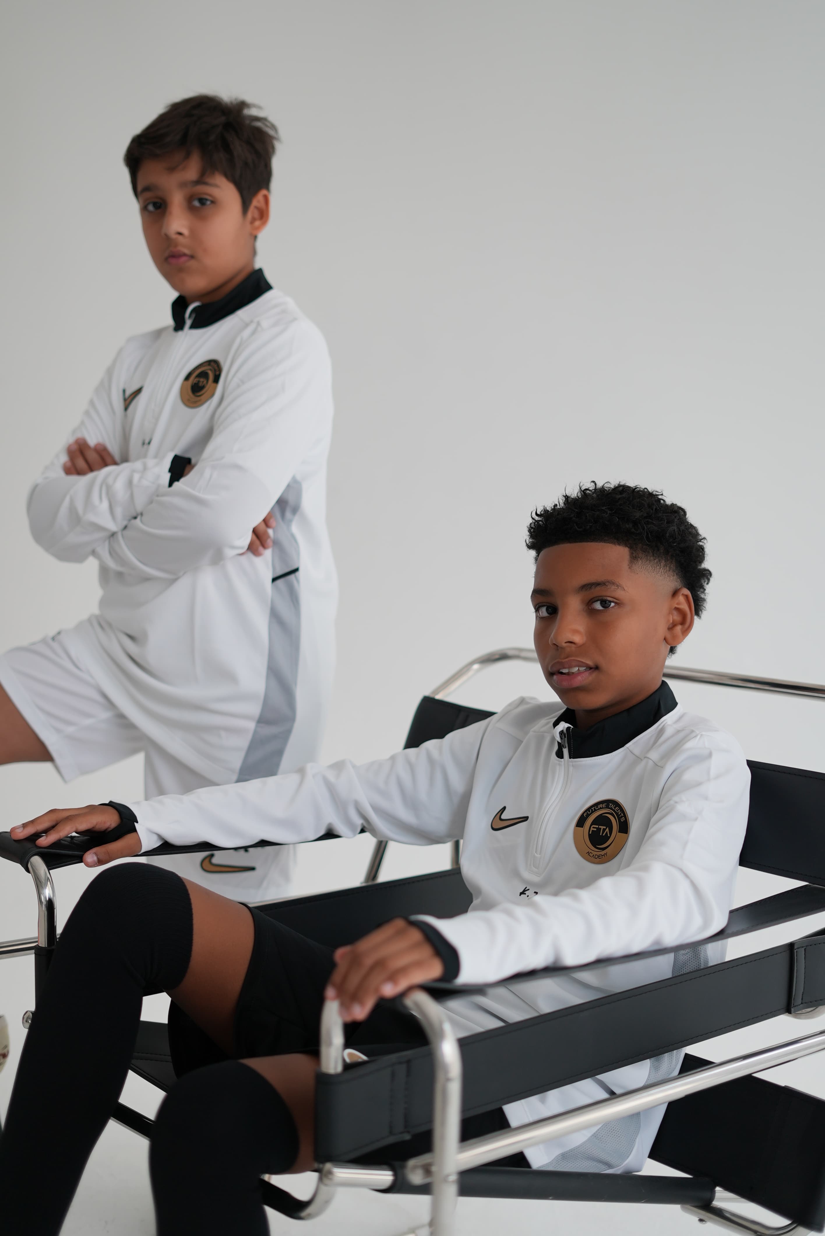 Two academy players in white and gold FTA tracksuits, seated for a studio portrait
